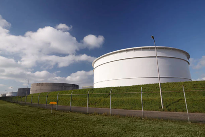 Overview of a petrochemical storage tank farm in Rotterdam, showing large cylindrical tanks with venting systems amid industrial infrastructure.